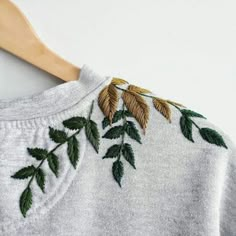 a white sweater with green leaves on it and a wooden hanger in the background