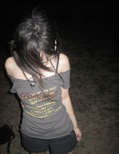 a young woman standing in the dark with her back turned to the camera and looking down