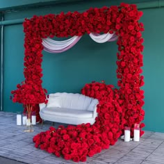 a white couch sitting in front of a red flower covered arch with roses on it