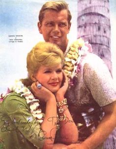 the man and woman are posing together in front of a palm tree