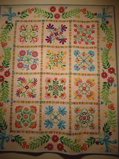 a colorful quilt with flowers and leaves on the front is hanging from a white wall