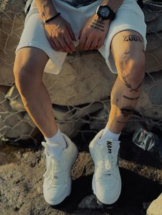 a man with tattoos sitting on a rock next to a netted area and wearing white sneakers