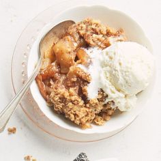 an apple crisp with ice cream in a white bowl on a table next to a spoon