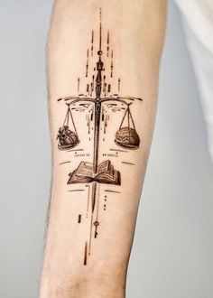 a tattoo on the arm of a person with a book and scales in front of them