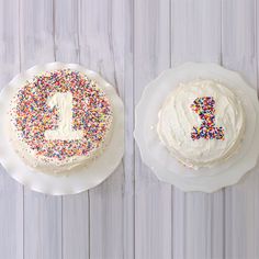 two cakes with white frosting and colorful sprinkles on them, one has a 1