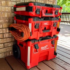 a stack of red tool boxes sitting on top of a wooden floor next to a brick wall