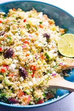 a blue bowl filled with rice and veggies next to a wooden spoon on top of a table