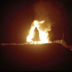 a person standing in front of a fire with bright orange flames coming out of it