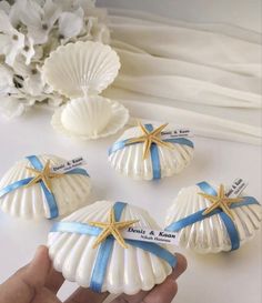 three seashells with blue ribbon and starfish on them are being held by a hand