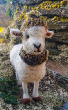 a stuffed sheep wearing a knitted hat and scarf on top of mossy ground