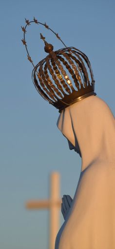 a statue with a crown on it's head and a cross in the background