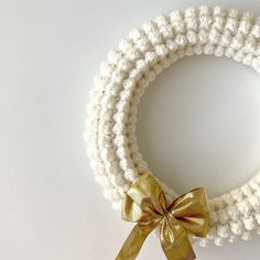 a crocheted bracelet with a gold bow on the front and white beads around it