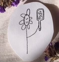 a white rock with a drawing of a flower and a phone on it next to purple flowers