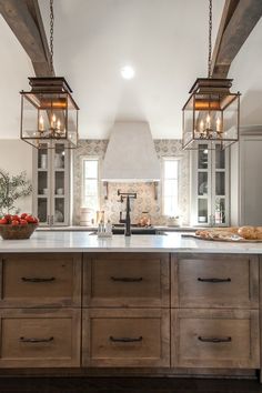 a kitchen with two hanging lights over the stove top and an island in front of it