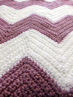 a crocheted blanket is laying on top of a bed with purple and white colors