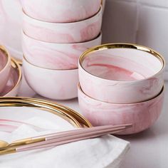 pink marble plates with gold rims are stacked on top of each other, along with chopsticks