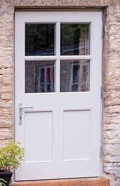 a white door sitting next to a window on top of a wooden bench in front of a stone building