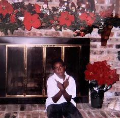 a man sitting in front of a fireplace with his hands crossed and flowers on the mantle