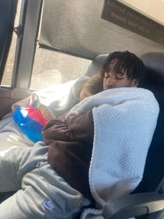 a young boy sleeping in a seat on a bus with his head covered by a blanket