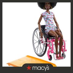 a doll in a wheel chair with an orange mat on the floor and text that reads,