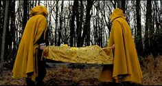 two people dressed in yellow robes holding a large piece of cloth with trees in the background