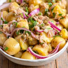 a white bowl filled with potatoes, onions and meat on top of a wooden table