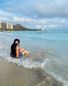 a woman sitting in the water on top of a sandy beach next to the ocean