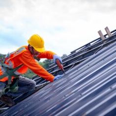 a man in an orange safety vest working on the roof of a building with metal shingles