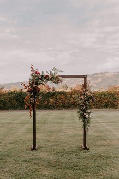 an outdoor ceremony set up with flowers and greenery on the top of wooden poles