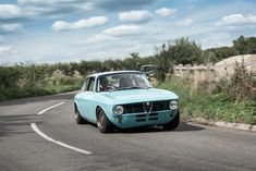 an old blue car driving down the road