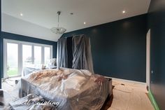 an empty room with blue walls and plastic covering the bed in the foreground is being worked on