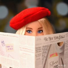 a barbie doll wearing a red beret reading a news paper