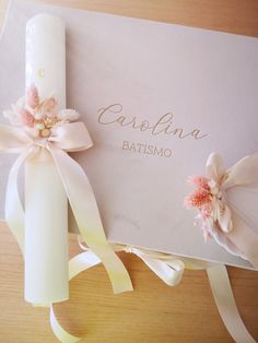 an open card with ribbon and flowers on the front, next to a candle that reads carolina batismo