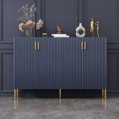 a blue cabinet with gold handles and some vases on the top, against a gray wall