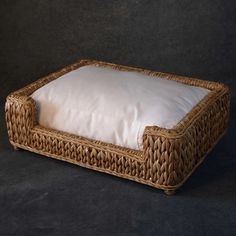 a wicker dog bed with a white pillow on it's back and sides