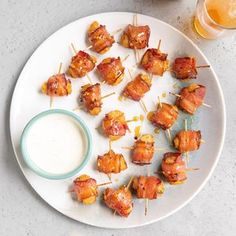 a white plate topped with bacon wrapped skewers next to a glass of beer