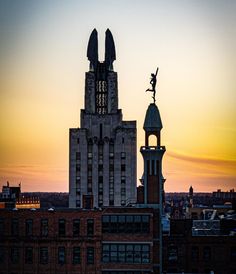 the top of a building with a statue on it's roof in front of an orange and blue sky