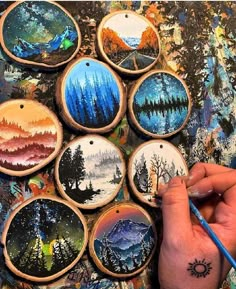 a person is holding a paintbrush and drawing on some painted wooden ornaments with mountains in the background