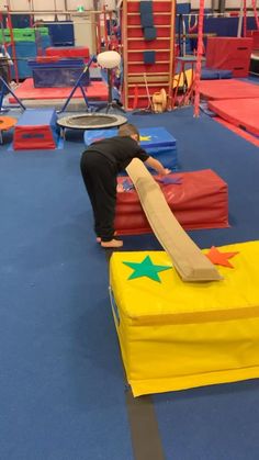 a person standing on top of a yellow box in a gym filled with gymnastics equipment