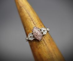 a pink diamond ring sitting on top of a wooden stick