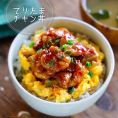 a bowl filled with meat and rice on top of a wooden table next to chopsticks