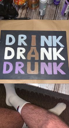 a man sitting on the floor holding up a sign that says drink drank and drunk