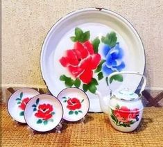 three plates with red and blue flowers on them next to a teapot, cup and saucer