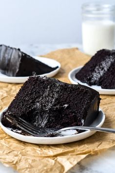 two white plates with slices of chocolate cake on them and a glass of milk in the background