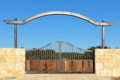 an iron gate with wooden posts in front of a stone wall and fenced entrance