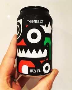 a hand holding a can of the fabulist hazy ipa with an evil face on it