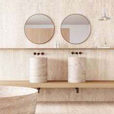 two round mirrors are on the wall above three white vases and a wooden bench