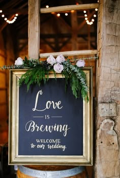 a sign that says love is brewing welcome to our wedding hanging on a barrel with flowers and greenery