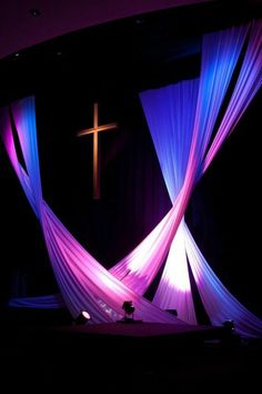 a cross on the side of a stage with purple and blue drapes draped over it