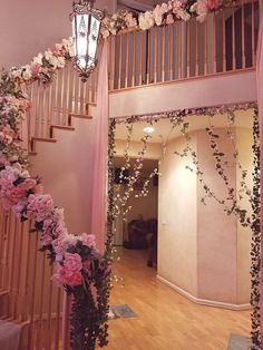 a staircase decorated with pink flowers and greenery next to a chandelier hanging from the ceiling